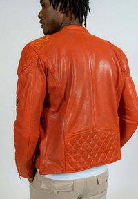 Veste en cuir rouge avec un dos texturé matelassé, finition lisse et coutures détaillées. Présente des zips et des accents sur les épaules.