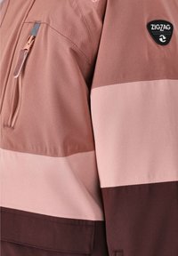 Veste bicolore rose et marron avec une poche poitrine zippée, des poignets élastiques et un patch logo Zigzag sur l'épaule.