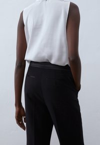 Vitt ärmlöst linne med en slät textur, kombinerat med svarta smala byxor med bakfickor och en midjeresår som framhäver midjan.