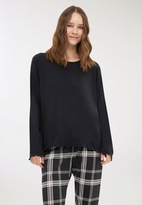 Maglietta nera a maniche lunghe con texture a coste e orlo scallop, abbinata a pantaloni a quadri bianco e nero con un motivo a scacchi.