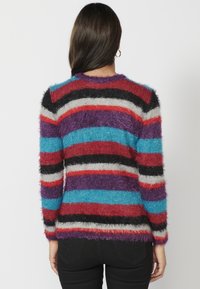 Pull rayé avec une texture douce et duveteuse dans les couleurs : rouge, noir, violet, turquoise et gris. Poignets et ourlet côtelés.