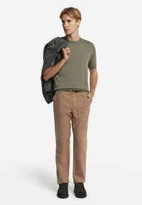 Kortärmad olivgrön stickad tröja, beige byxor med framfickor och svarta skor. En grå jacka hängande över armen.