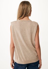 Maglione senza maniche beige con scollatura a girocollo, texture morbida e orlo a coste. Indossato sopra un paio di jeans in denim con un fit rilassato.