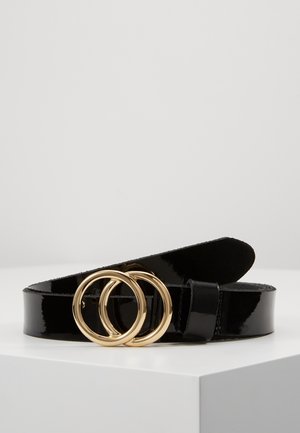 Black patent leather belt with double gold circular buckle resting on a white surface against a plain background.