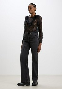 Top in pizzo nero con scollo arricciato abbinato a jeans neri a vita alta con applicazioni di strass e design a gamba dritta.