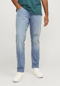 Light blue denim jeans with a straight-leg fit, featuring front pockets and a clean finish, paired with white sneakers.