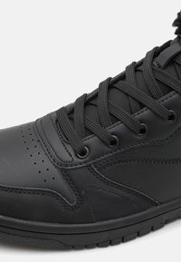 Zapatilla negra con un upper de cuero suave, puntera redonda, acentos texturizados y cordones negros pasados por ojales de metal. Detalles perforados presentes.