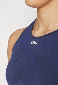 Top atlético de color azul marino con un cuello alto y una textura sutil, con un logo blanco en el pecho. Diseñado para la comodidad y la movilidad.