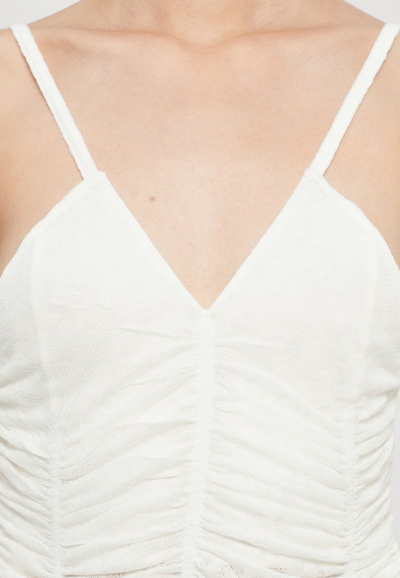 Top bianco senza maniche con scollatura a V, caratterizzato da un tessuto arricciato e sottile. Il design enfatizza una silhouette liscia e aderente.