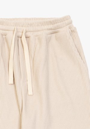 Pantaloni della tuta a coste leggeri beige chiaro con cintura elastica, cordoncino regolabile e tasche laterali. Tessuto morbido e vestibilità rilassata.