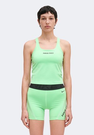 Kvinde iført lysegrøn Nike Pro ærmeløs top og matchende shorts med sort taljebånd, stående mod en ensfarvet baggrund og vendt fremad.