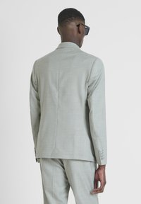 Giacca da abito grigia chiara con una texture liscia, vestibilità su misura e chiusura a un bottone; presenta tre bottoni su ciascun polsino.