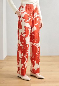 Wide-leg trousers in a cream fabric featuring bold red floral patterns. Elastic waistband and side pockets; smooth, lightweight texture.
