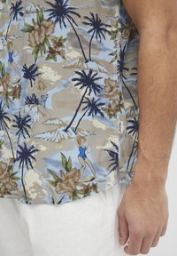 Cămașă cu mânecă scurtă dintr-un material bej deschis, având un model tropical cu figuri albastre înotând, flori și palmieri. Design texturat, casual.