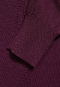 Fialový pletený svetr s žebrovanými manžetami a texturovaným tělem. Měkká, hladká látka vykazuje jednotný vzhled a mírný lesk.