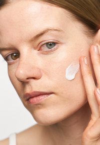 Facial moisturizer application on skin; creamy white texture on cheek. Smooth, hydrated skin with natural complexion and minimal blemishes.