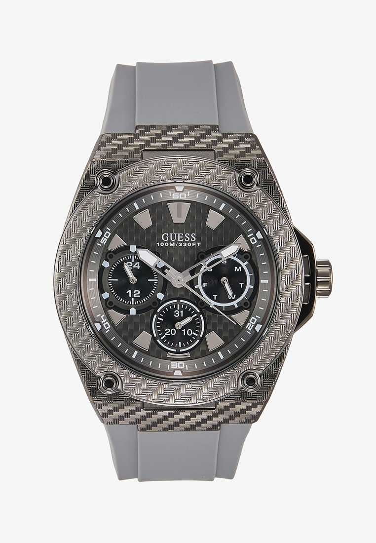 Montre-bracelet GUESS avec bracelet en silicone gris, lunette argentée texturée, cadran noir, trois sous-cadrans, et aiguilles ainsi que marqueurs d'heure argentés.