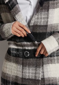 Wollen plaid jas met grijs, zwart en witte kleuren. Gestructureerde stof met zichtbare stiksels en grote zwarte knopen aan de voorkant.