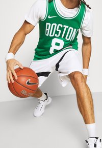 Jugador de baloncesto driblando un balón de baloncesto Nike, vistiendo una camiseta verde de Boston con el número 8 y pantalones cortos blancos con detalles en negro.