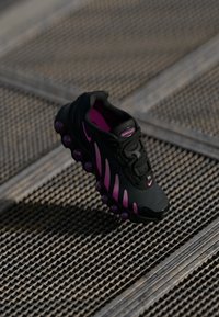 Black athletic shoe with pink accents, featuring a textured upper, prominent sole with air bubble detailing, and lacing system.