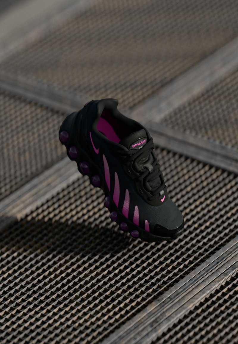 Black athletic shoe with pink accents, featuring a textured upper, prominent sole with air bubble detailing, and lacing system.
