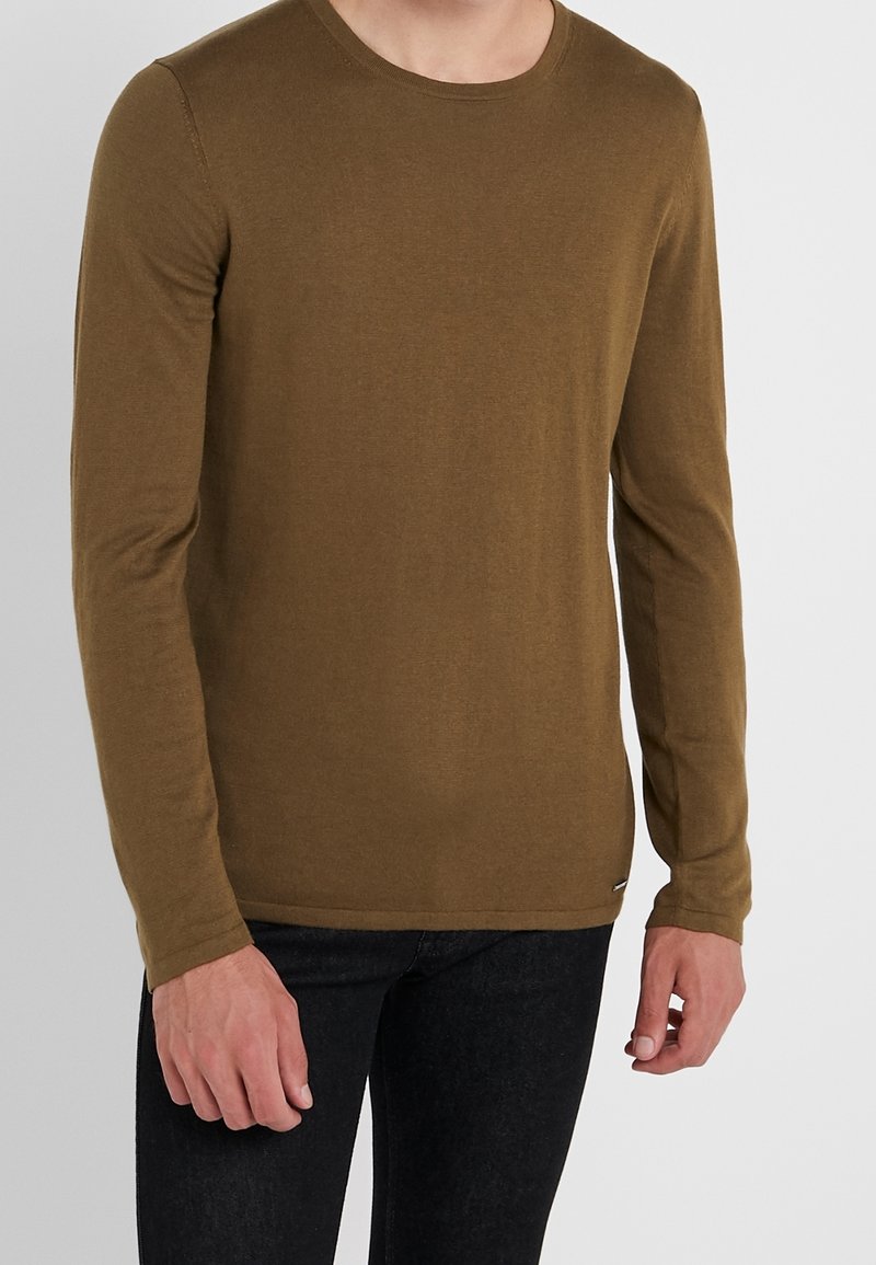 Langarmshirt aus olivgrünem Baumwollstoff, runder Ausschnitt, taillierter Schnitt, glatte Textur, mit einem kleinen Etikett-Detail am Saum.