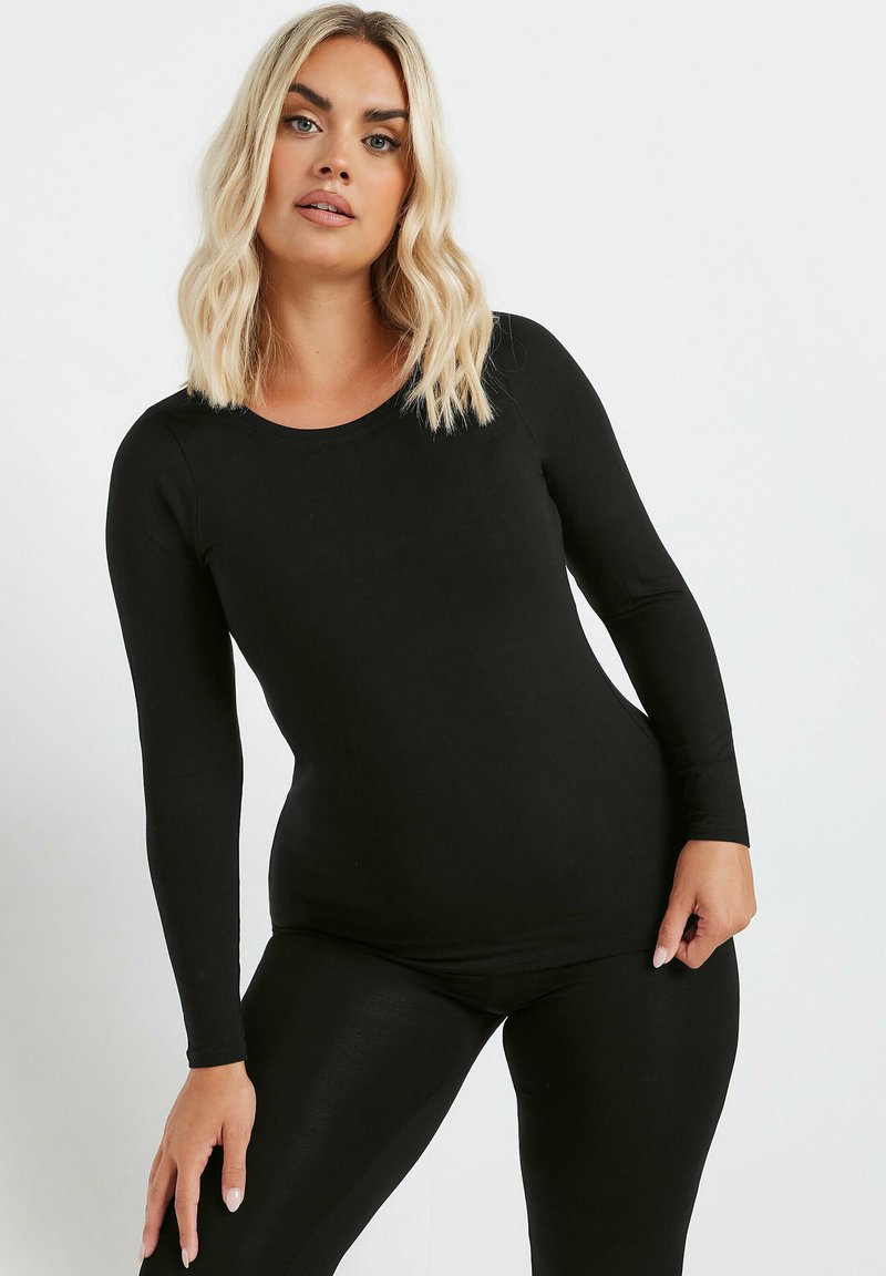 Zwarte longsleeve bodysuit gemaakt van een gladde, rekbare stof met een ronde halslijn. Het aansluitende ontwerp contrasteert met de losse legging-uitsnede.