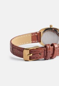 Brun lærrem med teksturert overflate, utstyrt med gullmetallspenne og flere justeringshull for tilpasning.