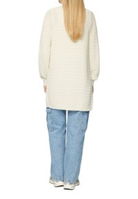 Crème sweater met lange mouwen, textuur en een ontspannen pasvorm, gecombineerd met lichtblauwe baggy jeans en witte sneakers, gezien vanaf de achterkant.