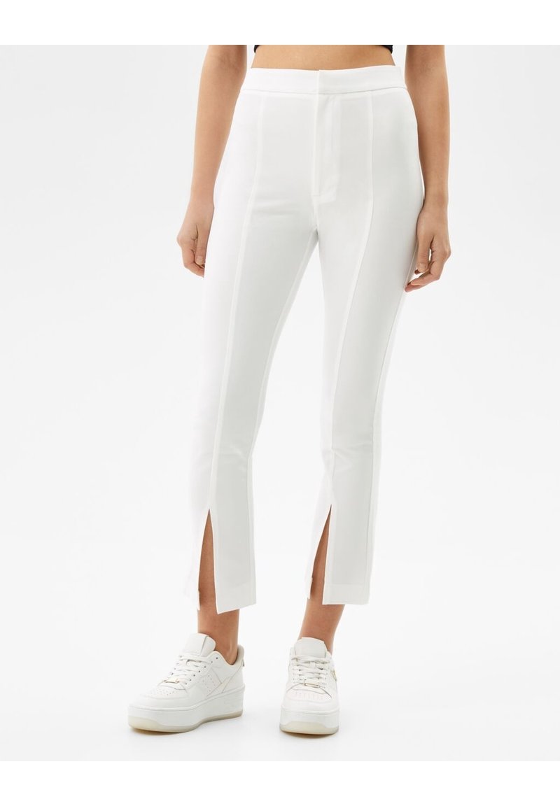 Vita figurnära byxor med sidoknäppningar i fållen, med en jämn textur och en skräddarsydd design. I kombination med vita sneakers.