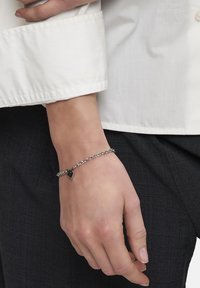 Zilveren kettingarmband met een klein hangslotje. De ketting heeft een gladde textuur en het ontwerp is minimalistisch en modern.