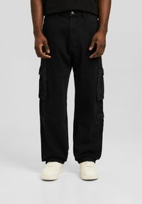 Czarne spodnie cargo wykonane z denimu. Luźny fason z wieloma bocznymi kieszeniami i zapięciem na guziki. W połączeniu z białymi trampkami z fakturowanymi detalami.