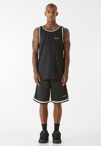 Melns sporta topiņš ar baltu apdari un logo, apvienots ar melnām biksēm, kurām ir baltas akcents. Nēsāts ar melnām kurpēm un zeķēm.