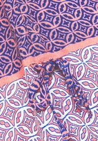 Tela con patrón geométrico en azul y naranja, con un detalle de lazo atado y una banda naranja horizontal que separa dos secciones estampadas.