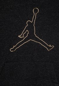 Čierna mikina s kapucňou so zlatým obrysom skáčucej postavy s basketbalovou loptou. Mäkká textúra, predná vrecko a minimalistický dizajn.