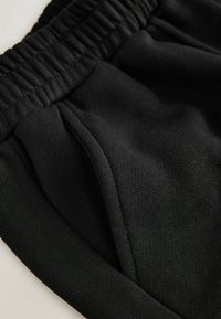 Černé sportovní šortky s elastickým pasem, strukturální tkaninou a bočními kapsami pro uložení. Detailní pohled ukazuje detaily materiálu.