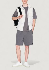 Chaleco acolchado blanco ligero sobre una camiseta gris y pantalones cortos a juego. Zapatillas blancas y un bolso negro completan el conjunto. Diseño simple y moderno.