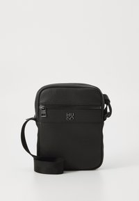 Geantă crossbody din piele neagră, cu o suprafață texturată, buzunar frontal cu fermoar, curea ajustabilă și detalii cu logo embossat. Formă rectangulară compactă.