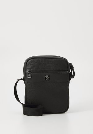 Sac en cuir noir porté croisé avec une surface texturée, poche zippée à l'avant, bandoulière réglable et détail en relief du logo. Forme rectangulaire compacte.