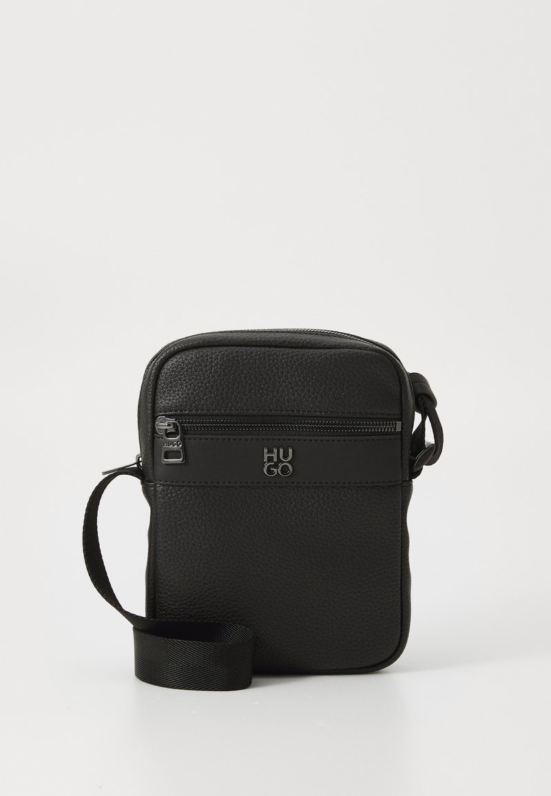 Geantă crossbody din piele neagră, cu o suprafață texturată, buzunar frontal cu fermoar, curea ajustabilă și detalii cu logo embossat. Formă rectangulară compactă.