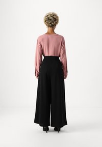 Růžový top s dlouhým rukávem v kombinaci s černými kalhotami s vysokým pasem a širokými nohavicemi. Hladké materiály, jednoduchý design a decentní švy.