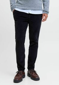 Ciemnoniebieskie spodnie z kordurojowego materiału z pionowym prążkowaniem, slim fit, w połączeniu z brązowymi skórzanymi butami. Sweter jest szary i ma długie rękawy.