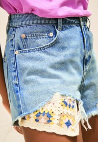 Jeansshorts met een rafelige zoom en een lichte wassing, met zichtbare zakken en een kleurrijke gehaakte rand die van onderaf tevoorschijn komt.