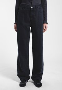 Tummansinisiä leveälahkeisia housuja, jotka on valmistettu puuvilladenimistä. Ne sisältävät suuret etutaskut, näkyvää ompelua ja korkeaa vyötärödesignia.