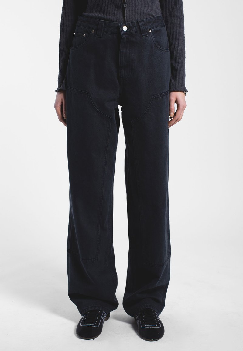 Tummansinisiä leveälahkeisia housuja, jotka on valmistettu puuvilladenimistä. Ne sisältävät suuret etutaskut, näkyvää ompelua ja korkeaa vyötärödesignia.