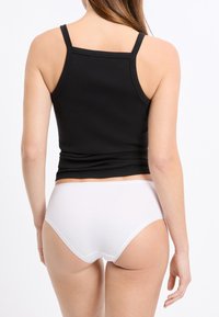 Canotta nera a costine con spalline sottili, abbinata a slip bianchi a vita alta, che mostrano una texture liscia e un design semplice visto da dietro.