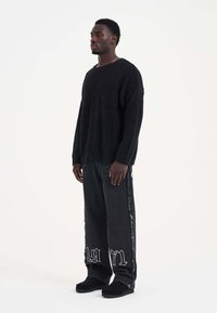 Zwarte fuzzy trui gecombineerd met losse zwarte jeans met rafelige details en een witte grafische print, aangevuld met zwarte instappers.