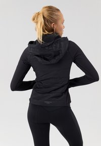 Must värvi aktiivne jakk, millel on kapuuts, sile eesmine osa ja tekstuuriga tagapaneel. Slim fit ja minimatlistlik disain.