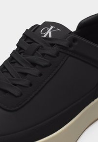 Μαύρο αθλητικό παπούτσι χαμηλού προφίλ με μαύρα κορδόνια, μαύρες ραφές, λογότυπο "cK" σε λευκό στο γλώσσιο και σόλα σε κρεμ απόχρωση.