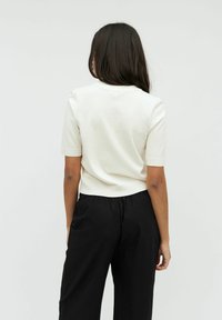 Hvid kortærmet top med tætsiddende design, kombineret med løse sorte bukser. Glat, strikket tekstur; enkel, minimalistisk stil.